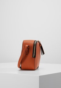 Borsa in pelle arancione con finitura testurizzata, chiusura laterale con zip, una tracolla corta e un tirazip decorativo. Forma compatta rettangolare.