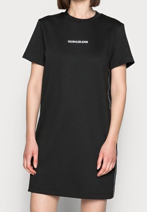 Kvinde iført en sort kortærmet Calvin Klein Jeans t-shirt kjole med hvidt logo centreret på brystet.