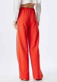 Heldere oranje sweatpants met een ontspannen pasvorm, elastische tailleband en witte zijkanten. Zachte textuur, geschikt voor casual draag.