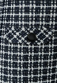 Marineblaues und weißes gemustertes Gewebe mit strukturiertem Webmuster, ausgestattet mit einem schwarzen Knopf auf einer diagonal platzierten Klapptasche.