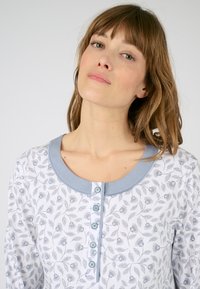 Camisa de pijama de manga larga en algodón blanco con un patrón floral en azul. Cuenta con un cuello azul claro y una tapeta de seis botones con botones redondos.