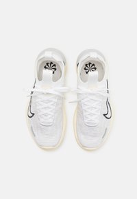 Paire de chaussures de sport blanches en maille avec logos Swoosh noirs, lacets blancs, semelles beiges et semelles intérieures à motif floral, vues de dessus.