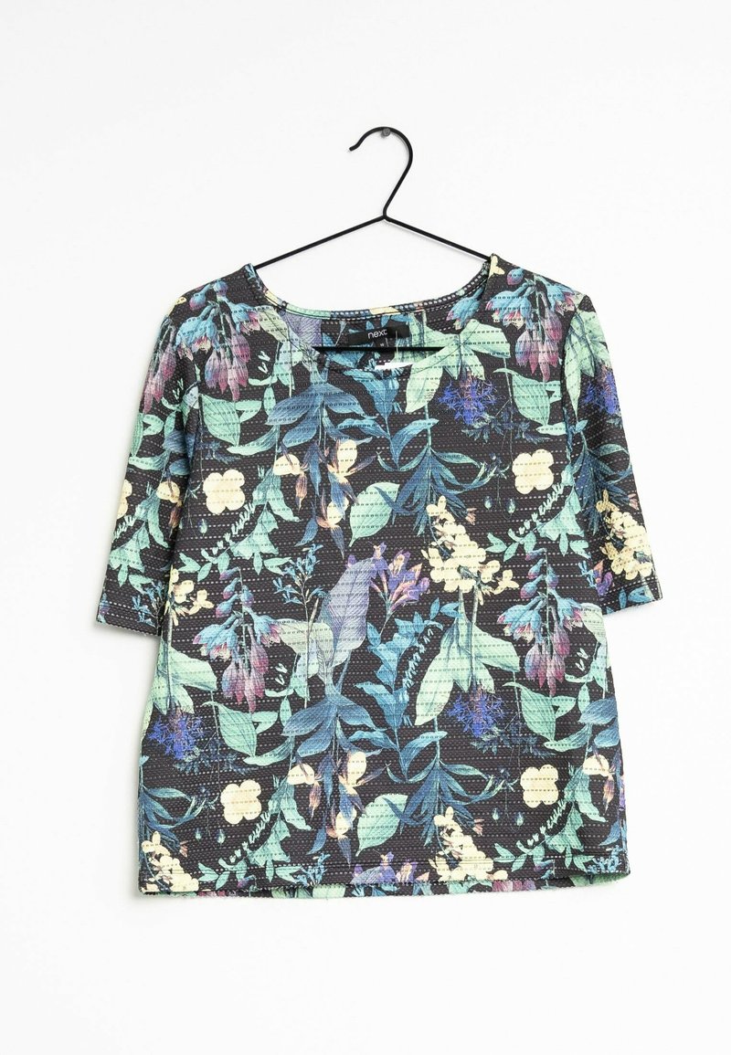 Chemise noire à manches courtes avec des motifs floraux et de feuilles verts, bleus, violets et crème, suspendue sur un cintre en fil noir sur fond blanc.