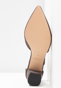 Vue de dessous d'une chaussure plate en daim gris à bout pointu avec talon noir et nom de la marque "Kurt Geiger London" imprimé sur la semelle.