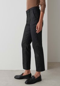 Black straight-leg jeans with a high waist, featuring side pockets and subtle stitching details. Worn with black loafers and a brown top.