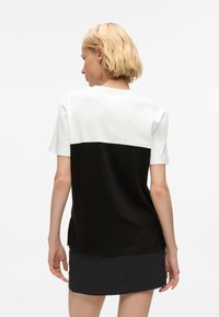 T-shirt z krótkim rękawem w designie z blokami kolorów; górna połowa biała, dolna połowa czarna. Materiał wydaje się miękki o gładkiej fakturze.