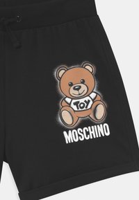 Pantalones cortos negros de algodón con un gráfico de un oso de dibujos animados, camiseta blanca con la palabra "Toy" y el texto "Moschino" en letras blancas en negrita. Cintura con cordón ajustable.