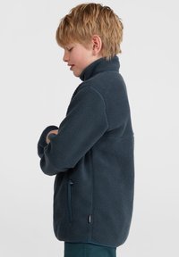 Tumedast meresinisest fleece-jakk kõrge krae, horisontaalsed tõmblukupocket'id ja tekstuuritud kangas. Omab regulaarset lõiget ja elastseid mansette.