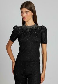 Czarny krótki top z krótkimi rękawami o błyszczącej strukturze, z marszczonym dekoltem i błyszczącymi akcentami na całej powierzchni. Dopasowany krój.