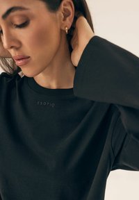 Czarny sweatshirt z okrągłym dekoltem, z delikatnym logo marki na piersi oraz długimi, gładkimi rękawami w luźnym kroju.