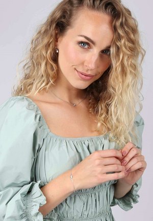 Zilveren armband met een verfijnd ontwerp, gedragen door een model in een mintgroene top met pofmouwen, die een ontspannen, gestructureerde stof tentoonstelt.