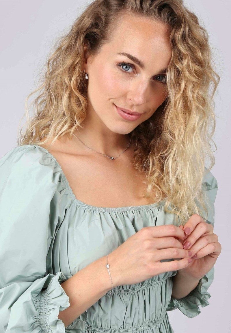 Zilveren armband met een verfijnd ontwerp, gedragen door een model in een mintgroene top met pofmouwen, die een ontspannen, gestructureerde stof tentoonstelt.