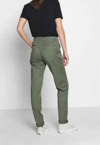 Groene katoenen chino's met een getailleerd ontwerp, voorzien van achterzakken en omgeslagen pijpen, gecombineerd met witte sneakers en een zwart T-shirt.