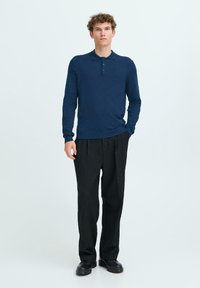 Polo de manga larga en color navy con tapeta de tres botones, fabricado con tejido texturizado. Combinado con pantalones negros de corte holgado y zapatos negros.
