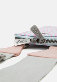 Zipperowa saszetka w jasnoniebieskim kolorze w różowe kropki, z metalowymi zamkami i skórzanymi akcentami. Teksturowany materiał i kontrastowe kolorowe detale.