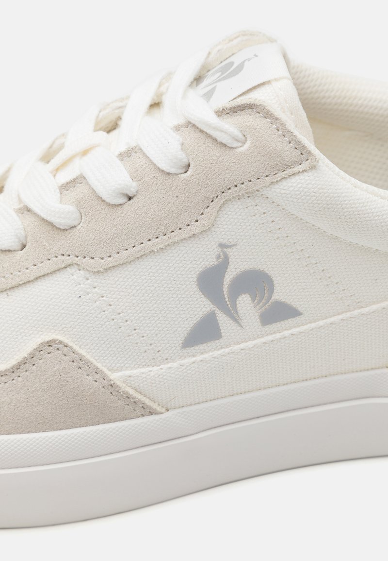 Baskets blanches avec des accents gris, en toile et en daim, à bout arrondi, fermeture à lacets et détail de logo sur le côté.
