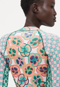 Flerfarget rash guard med blomstermønstre og stjerner, i sterke rosa, grønn og blå nyanser; glatt stoff og flatlock-søm.