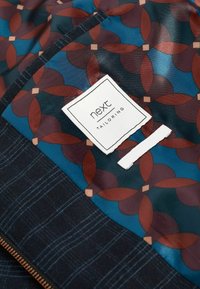 Tailored jacket interior with a glossy blue fabric featuring a burgundy and brown geometric pattern. Includes a white label tagged 'next.'