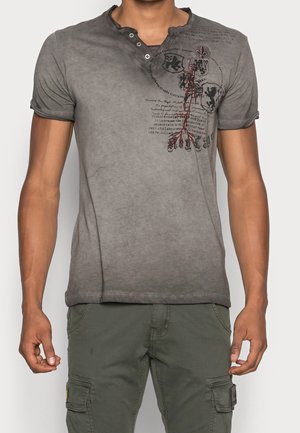 T-shirt gris en coton avec un effet délavé, col rond, patte de boutonnage à deux boutons et motif sérigraphié en noir et rouge sur le devant.