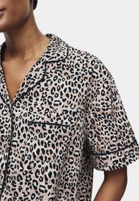 Koszula nocna w leopardzi wzór z miękkiego materiału, z kołnierzykiem, krótkimi rękawami, czarnymi wykończeniami i gładką kieszonką na piersi.