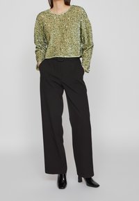 Zielony sweter z cekinami, z długimi rękawami i okrągłym dekoltem; zestawiony z czarnymi spodniami o szerokich nogawkach i czarnymi botkami za kostkę.