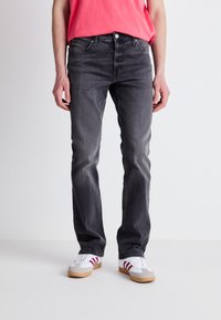 Jeans de mezclilla gris con un corte ajustado, que presentan un diseño clásico de cinco bolsillos, un sutil desgaste y costuras en contraste. Combinados con zapatillas blancas.