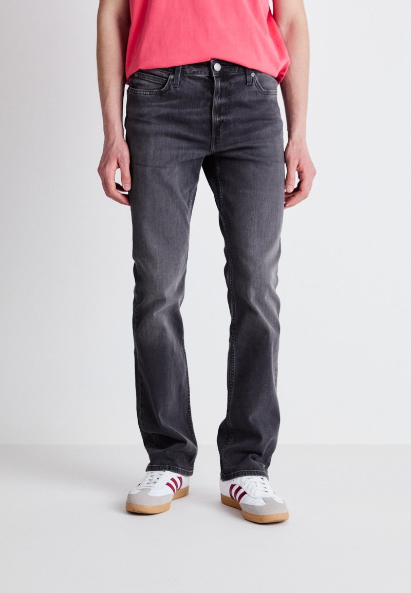 Jeans de mezclilla gris con un corte ajustado, que presentan un diseño clásico de cinco bolsillos, un sutil desgaste y costuras en contraste. Combinados con zapatillas blancas.
