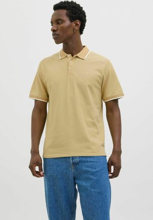 Polo en coton beige clair, avec un col classique, une patte de boutonnage à trois boutons et des finitions contrastantes sur le col et les manches.