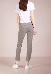 Šedé manšestrové kalhoty s úzkým střihem, dvěma zadními kapsami a zkrácenou délkou, zkombinované s bílými teniskami a jednoduchým bílým tričkem.