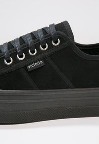 Sneaker nera in tela con una superficie testurizzata, suola in gomma e lacci scuri. Presenta occhielli in argento e un piccolo logo del marchio sul lato.