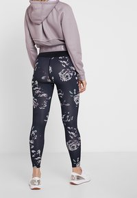 Lyhytlaventeliväri huppari, jossa on verkko-yksityiskohta, yhdistettyinä muotoileviin mustiin leggingseihin, joissa on kukkakuosi, ja valkoisiin lenkkikenkiin, joissa on metalliset yksityiskohdat.