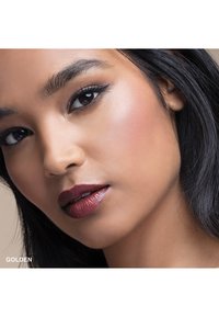 Le modèle cosmétique présente un teint chaud et lumineux avec un sous-ton doré. Des lèvres bordeaux audacieuses, un eyeliners bien défini et des cheveux noirs lisses.
