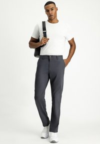 Pantalones gris oscuro con cierre de botón y bolsillos laterales, combinados con una camiseta blanca ajustada y zapatillas blancas. Bolso negro colgado del hombro.