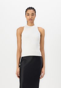 Top bianco a coste senza maniche con design a collo alto, forma aderente e tessuto testurizzato. Abbinato a una gonna nera in satin.