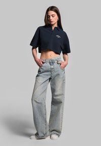 Granatowa, krótka koszulka polo z krótkim rękawem i haftowanym logo, w zestawie z jasnoniebieskimi spodniami typu wide-leg z przetarciami.