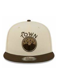 Beige Baseballcap mit einem dunkelbraunen flachen Schirm. Verfügt über ein gesticktes rundes Logo mit einem Baum und dem Schriftzug "The TOWN" darüber.