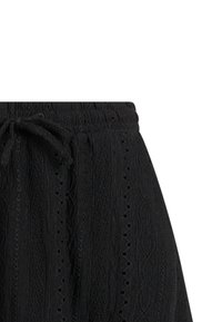 Čierne nohavice z textúrovaného materiálu s elastickým pásom a šnúrkou na zaväzovanie, zdobené vertikálnymi vzormi z očiek čipky.