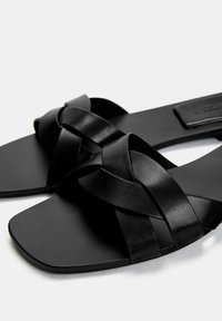 Schwarze flache Sandalen mit geflochtenen Lederriemen, quadratischem Zehenbereich und mattem Finish. Erhöhte Sohle für Komfort und Langlebigkeit.