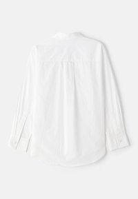Camicia bianca a maniche lunghe realizzata in un tessuto morbido, con polsini abbottonati, una piega sulla schiena, orlo curvo e un design con colletto classico.