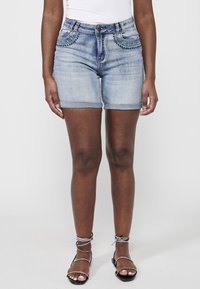 Shorts en jean de couleur bleu clair avec des perles décoratives et des sequins sur les poches, présentant une coupe ajustée et des ourlets repliés.