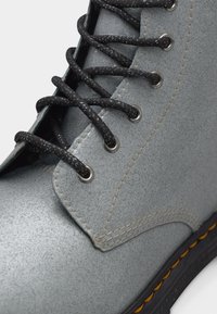 Κοντινό πλάνο γκρι δερμάτινου μποτάκι με υφή, με μαύρα κορδόνια με στίγματα, ασημένιες τρύπες για κορδόνια, λεπτομερείς ραφές και μαύρη σόλα με κίτρινες ραφές.