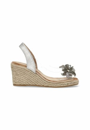 Sandalía de cuña con tacón metálico plateado, parte superior transparente y un adorno floral decorativo con detalles de cristal sobre una suela de yute trenzado.