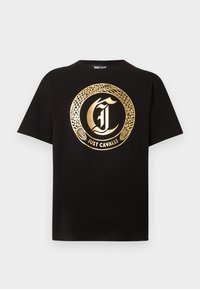 Μαύρο μπλουζάκι με κοντά μανίκια, με μεγάλο χρυσό κυκλικό σχέδιο φιδιού και διακοσμητικό γράμμα "J" στο κέντρο, με το κείμενο "JUST CAVALLI" από κάτω.