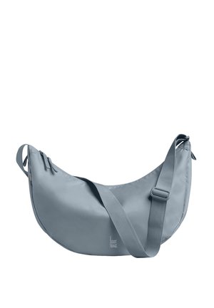 Lyseblå skuldertaske formet som en halvmåne med justerbar rem og lynlåslukning, præget med "GOT BAG" logo nær bunden i midten.
