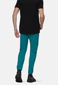 Zwart heren t-shirt gecombineerd met teal tapered joggingbroeken met elastische boorden en zwarte sportschoenen met gestructureerde zolen.