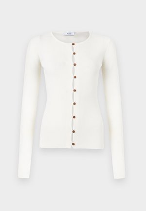 Hvit ribbestrikket cardigan med lange ermer, rund hals og åtte brune knapper foran.