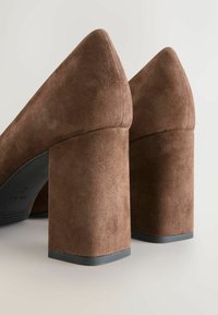 Paire de chaussures en daim marron pour femmes à talons blocs avec talons carrés arrondis et semelles en caoutchouc noir sur un fond clair.