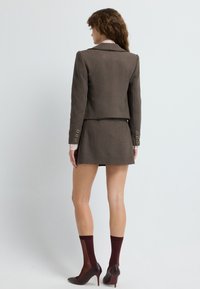 Brązowy garniturowy żakiet z pasującą spódnicą. Żakiet ma zbudowaną sylwetkę, klasyczne klapy i złote akcenty guzika. Połączony z burgundowymi skarpetkami i szpilkami.