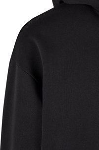 Felpa nera in tessuto morbido e strutturato. Presenta un cappuccio e un design con spalle scese, che enfatizza una forma rilassata e moderna.