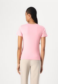 T-shirt ajusté en coton rose avec des manches courtes et un col rond, présentant une texture lisse et un design minimaliste.